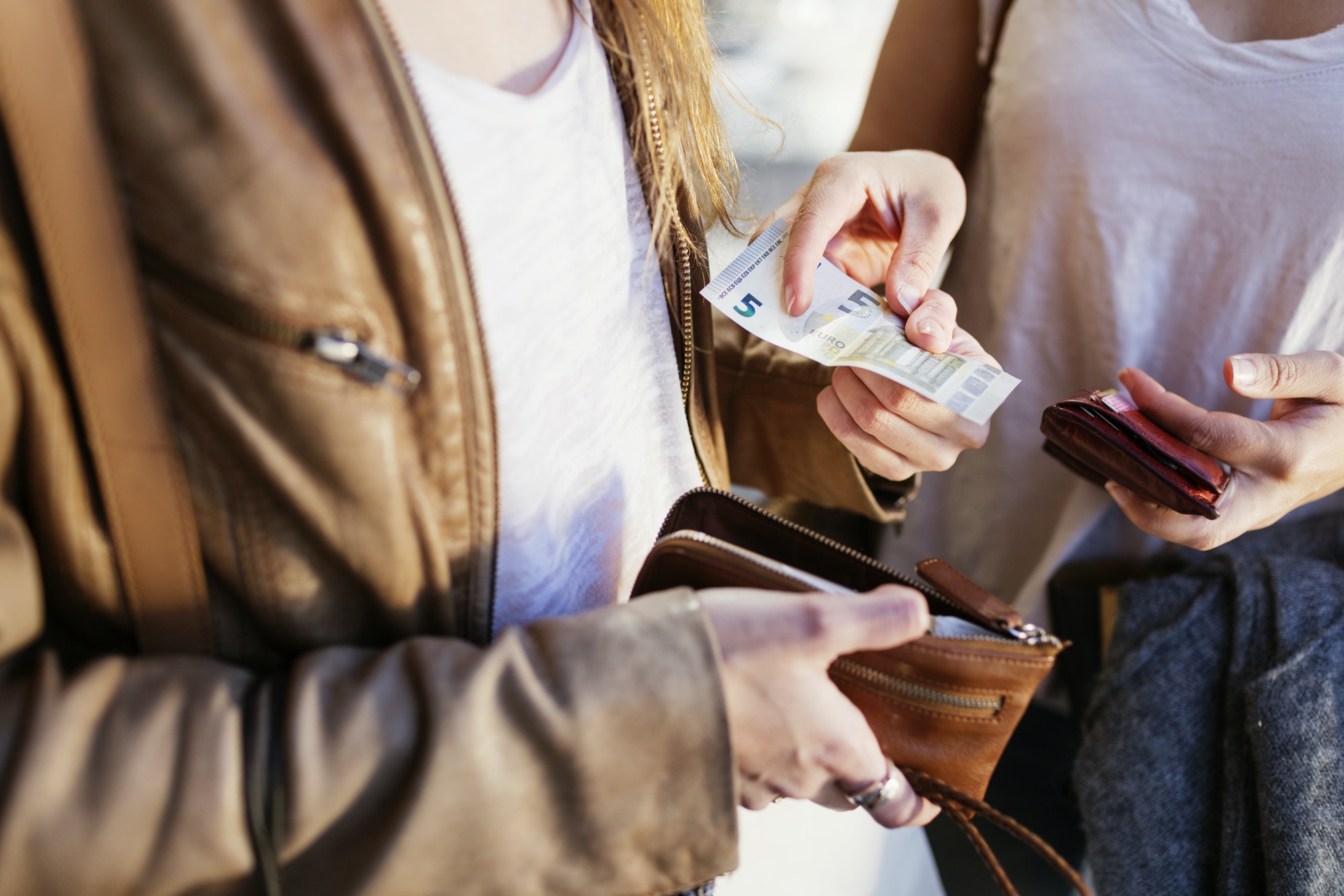 Midsection of woman giving five euro banknote to female friend outdoors